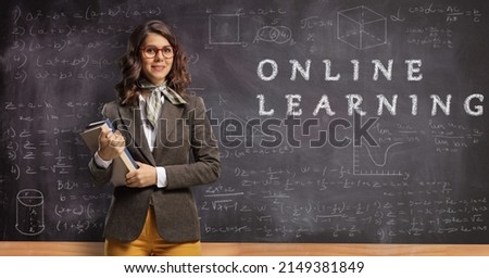 Young female teacher holding books and posing in front of a blackboard with text online learning
