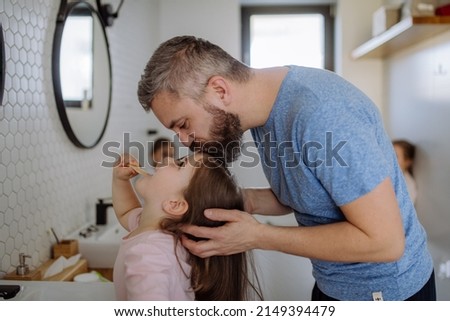 Father kissing his daughter while she is brushing her teeth in bathroom, morning routine concept.