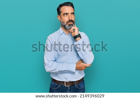 Middle aged man with beard wearing business shirt with hand on chin thinking about question, pensive expression. smiling and thoughtful face. doubt concept.  Royalty-Free Stock Photo #2149396029