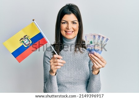Young hispanic woman holding colombia flag and colombian pesos banknotes smiling with a happy and cool smile on face. showing teeth. 