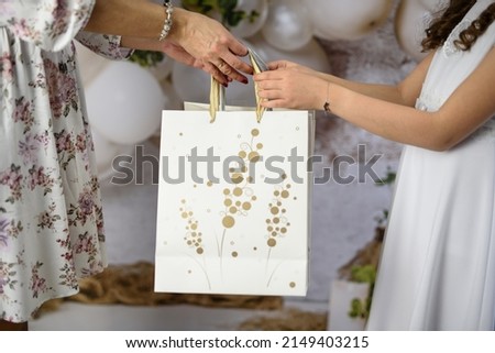 A gift from godparents for the first holy communion. A woman giving the girl a First Communion gift. First Communion gifts in decorative bags. Royalty-Free Stock Photo #2149403215
