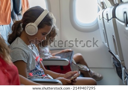 Kid schoolgirl in headphones watches cartoons in a phone on an airplane. little girl travels in an airplane, sitting in her seat, playing with a tablet computer, phone and headphones