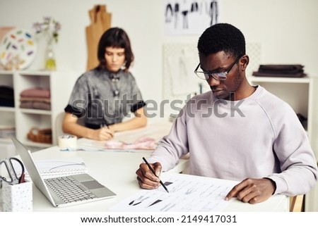 Serious Black young man creating fashion design sketches for his clothing line