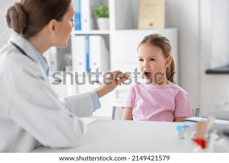 medicine, healthcare and pediatry concept - female doctor or pediatrician with tongue depressor checking little girl patient's throat on medical exam at clinic Royalty-Free Stock Photo #2149421579