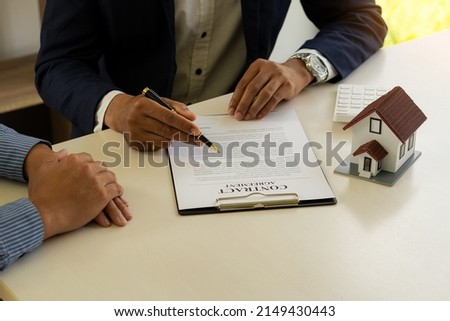 A real estate agent or bank officer explains the interest on a loan to clients with a home purchase contract and offers a title lease at the desk in the office. Royalty-Free Stock Photo #2149430443