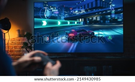 Close Up on Man's Hands at Home, Sitting on a Couch in Stylish Loft Apartment and Playing Arcade Car Video Games on Console. Male Using Controller to Play Street Racing Drift Simulator. Royalty-Free Stock Photo #2149430985