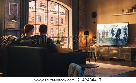 Authentic Couple Spending Time at Home, Sitting on a Couch and Watching Latest Blockbuster on Flat Screen Television Set. Man and Woman Streaming Movie or Show Using Home Cinema System. Royalty-Free Stock Photo #2149434417