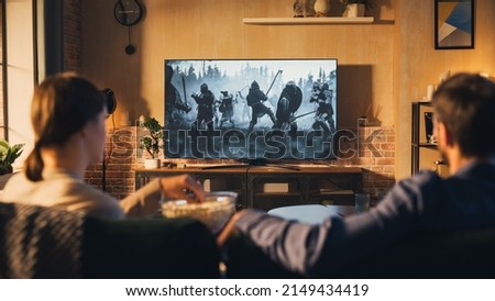 Authentic Couple Spending Time at Home, Sitting on a Couch and Watching Latest Blockbuster on Flat Screen Television Set. Man and Woman Streaming Movie or Show Using Home Cinema System. Royalty-Free Stock Photo #2149434419