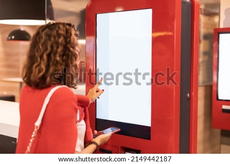 A girl orders food and lunch at a fast food restaurant using a self-service kiosk or a terminal with a screen. Modern commerce equipment Royalty-Free Stock Photo #2149442187