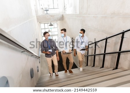 business, people and corporate concept - businessmen in masks with name tags walking up office stairs and talking