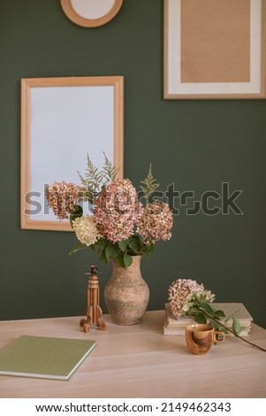 Home interior decor template with hydrangea flowers, books, wooden candle holder, handmade ceramic cup and various picture frames mock up on the wall.