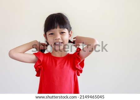 Portrait of Thai Asian kid girl, aged 4 to 6 years old, looks cute and smiles. wearing a red shirt She stood and put her hand on the hair behind her. Happy and bright, isolated white background
