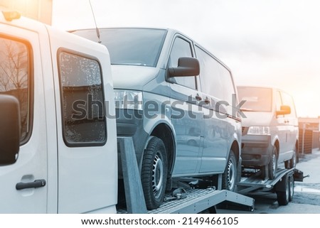 White small cargo truck car carrier loaded with two yellow van minibus on flatbed platform and semi trailer tow on roadside highway road. Volunteer support delivery transport for ukrainina people Royalty-Free Stock Photo #2149466105