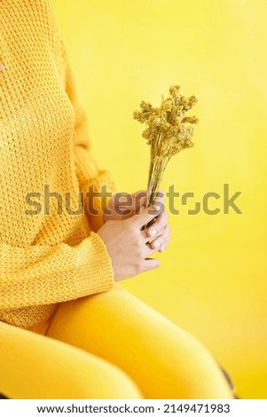 Woman with yellowish fashion style holding yellow dried baby breath flower. Creative monochrome yellow atmosphere.