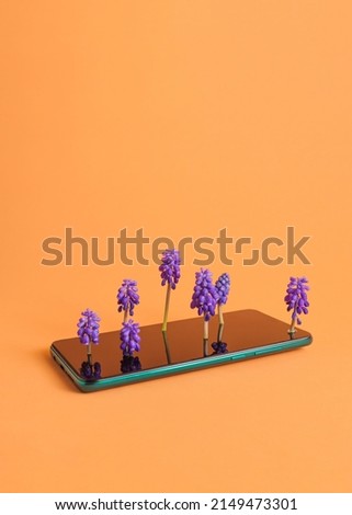 A phone with purple flowers growing from the screen. Orange background, front view. Minimalist idea. Free space on the top.
