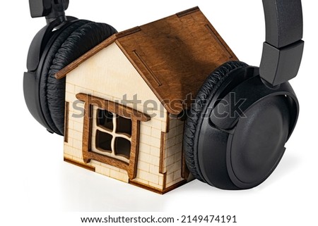 Black wireless  headphones on a small wooden house close up isolated on white background. Musical concept. Сoncept of soundproofing a house. 