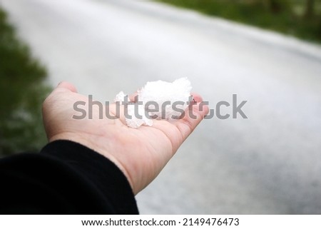 A man's hand holding snow in his hand after it snows against a snow-covered road in the background.