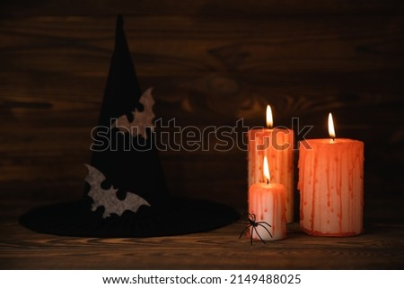 Composition of a group of scary bloody candles burning on a textured brown wood.Copy space on background.Witch hat with spider and bat. Black magic ritual or scary Halloween rite.DIY Halloween decor.