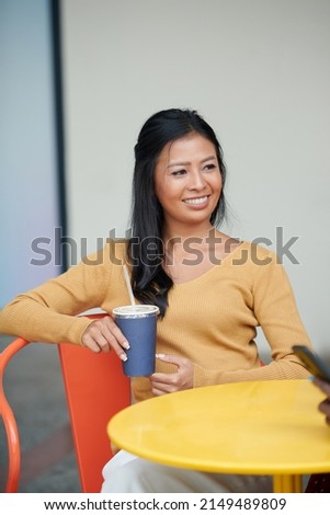 Portrait of elegant smiling young Asian woman enjoying cold drink in outdoor coffeeshop