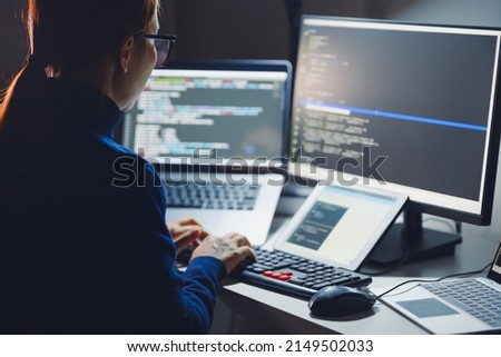 Young Asian woman, developer programmer, software engineer, IT support, wearing glasses working hard at nitght overtime on computer to check coding in bugging system. Back view Royalty-Free Stock Photo #2149502033