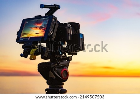 Professional camera on tripod taking picture film video of sunset over sea.