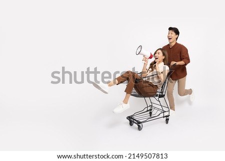 Asian woman sitting inside of shopping trolley and holding megaphone and Asian man pushing shopping cart isolated on white background, Announce sale concept Royalty-Free Stock Photo #2149507813