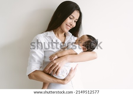 Beautiful young Asian mother and cute newborn son in her arms. Loving Asian mom hug embrace small baby child, relax enjoy tender family moment at home. Beautiful family, mother's day concept.