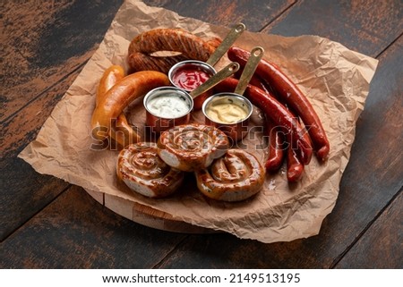A mix of grilled sausages - Bavarian, round, Cumberland, bratwurst with ketchup and sauce on a wooden table. Traditional Bavarian Beer Snack Royalty-Free Stock Photo #2149513195