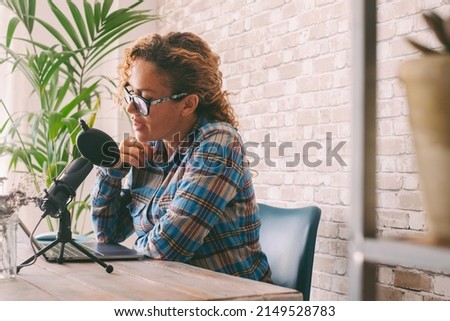 Content creator adult woman recording a podcast interview using microphone and laptop sitting at the desk. Home office workstation and smart working modern people lifestyle. Online radio computer job