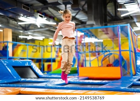 Pretty girl kid jumping on colorful trampoline at playground park and smiling. Caucasian preteen child during active entertaiments indoor Royalty-Free Stock Photo #2149538769