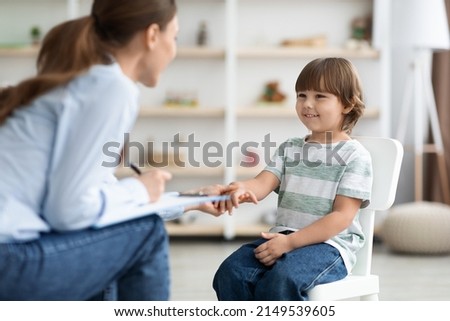 First meeting with patient. Friendly professional woman child psychologist greeting cute little boy, touching his hand and smiling at office Royalty-Free Stock Photo #2149539605