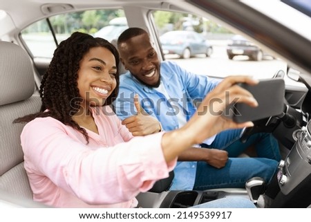 Beautiful young African American couple taking selfie inside car, using mobile phone, showing thumbs up sign gesture. Happy black man and woman going on vacation, taking self photo, buying new auto Royalty-Free Stock Photo #2149539917