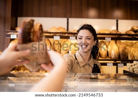 Beautiful smiling bakery worker selling pastry to the customer in bakery shop. Royalty-Free Stock Photo #2149546733