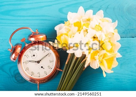 Vintage mechanical alarm clock with yellow daffodils on a blue wooden background. Fashion colors. Support for Ukraine. Colors of the Ukrainian flag. Good morning, we are from Ukraine