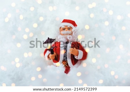 Toy doll Santa Claus on a white snowy background with space for text. Bright lights.