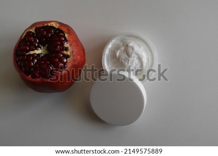 Cosmetic cream and whole pomegranate fruit on gray wood table background mockup with text space