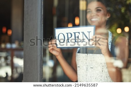 The best cafe in town is now open for business. Cropped shot of a young woman hanging up an open sign on the window of her cafe.