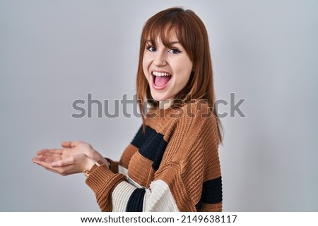 Young beautiful woman wearing striped sweater over isolated background pointing aside with hands open palms showing copy space, presenting advertisement smiling excited happy 