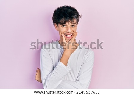 Handsome hipster young man wearing casual white shirt looking confident at the camera smiling with crossed arms and hand raised on chin. thinking positive. 