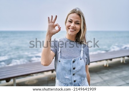 Young caucasian woman outdoors smiling positive doing ok sign with hand and fingers. successful expression. 