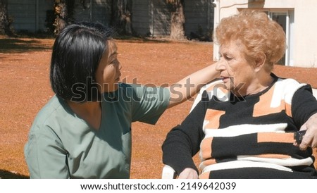 Young asian female doctor reassuring elderly retired woman, talking to her in the hospital garden.