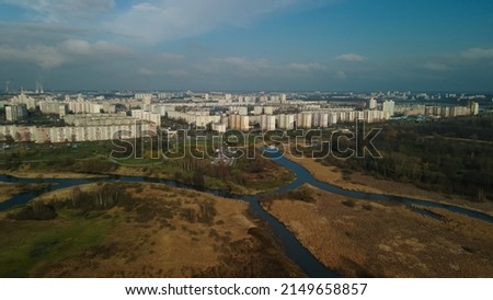 Flight over the spring city park. A river flows through the park. On the horizon there is a blue sky and city houses. Aerial photography.