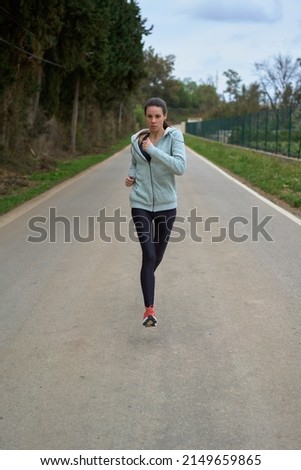 sportswoman running on a paved road through the forest front view with leggings and sweatshirt