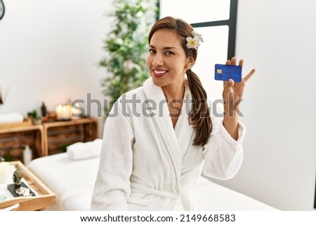 Young latin woman wearing bathrobe holding credit card 