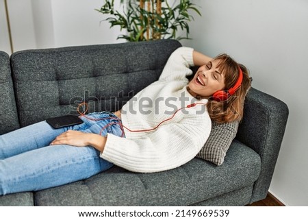 Young caucasian woman listening to music lying on sofa at home