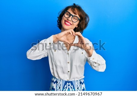 Young brunette woman wearing casual clothes and glasses smiling in love doing heart symbol shape with hands. romantic concept. 