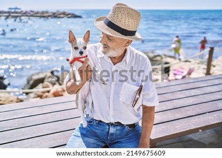 Senior man wearing summer hat hugging chihuahua at seaside