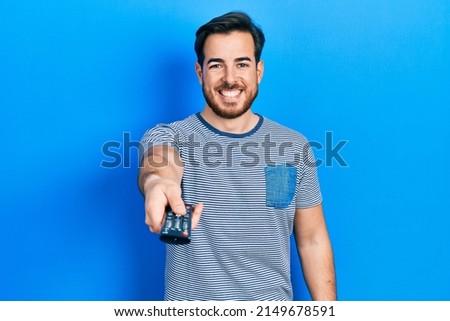 Handsome caucasian man with beard holding television remote control smiling and laughing hard out loud because funny crazy joke.  Royalty-Free Stock Photo #2149678591