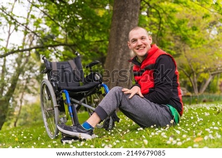 Disabled person in a public city park sitting in a wheelchair, smiling sitting on the grass with the spring flowers