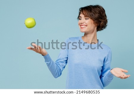 Young smiling satisfied happy vegetarian cool woman 20s in casual sweater look camera toss up green apple isolated on plain pastel light blue background studio portrait. People lifestyle food concept. Royalty-Free Stock Photo #2149680535
